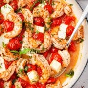 Close-up of baked shrimp with feta and tomatoes in a white skillet, garnished with fresh herbs.