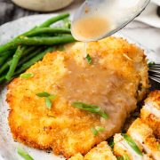 Spoon pouring lemon sauce over crispy breaded chicken cutlet, served with green beans.