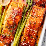 Gochujang-glazed salmon fillets baked with asparagus on a sheet pan, topped with sesame seeds, chopped green onions, and lemon slices.