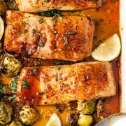 Sheet pan honey garlic salmon with roasted Brussels sprouts, garnished with lemon wedges and fresh herbs.
