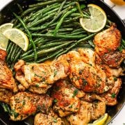 Skillet with juicy cowboy butter chicken thighs and crisp green beans, garnished with fresh parsley and lemon slices.