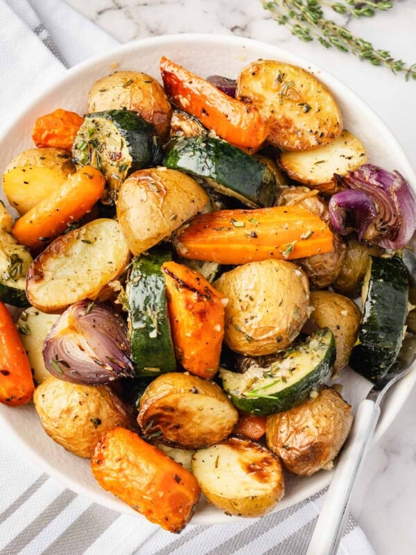 Bowl of garlic herb roasted potatoes, carrots, zucchini, and red onion—golden, crispy, and oven-roasted.