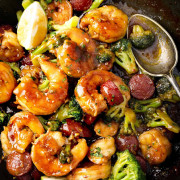 Honey garlic shrimp, sausage, and broccoli in a skillet with lime wedges and glossy sauce.