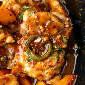 Close-up of Jalapeno Peach Chicken with peach slices, jalapeno, and glossy peach glaze in a skillet.