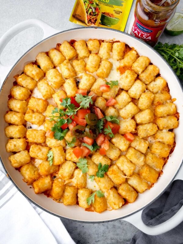 Fiesta Chicken Tater Tot Casserole baked in a white skillet, topped with cheese, salsa, jalapeรฑos, and cilantro.