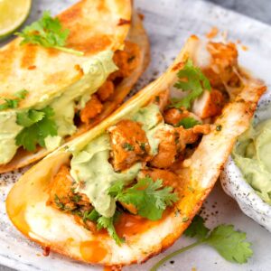 Crispy buffalo chicken tacos with avocado crema and fresh cilantro on a plate.