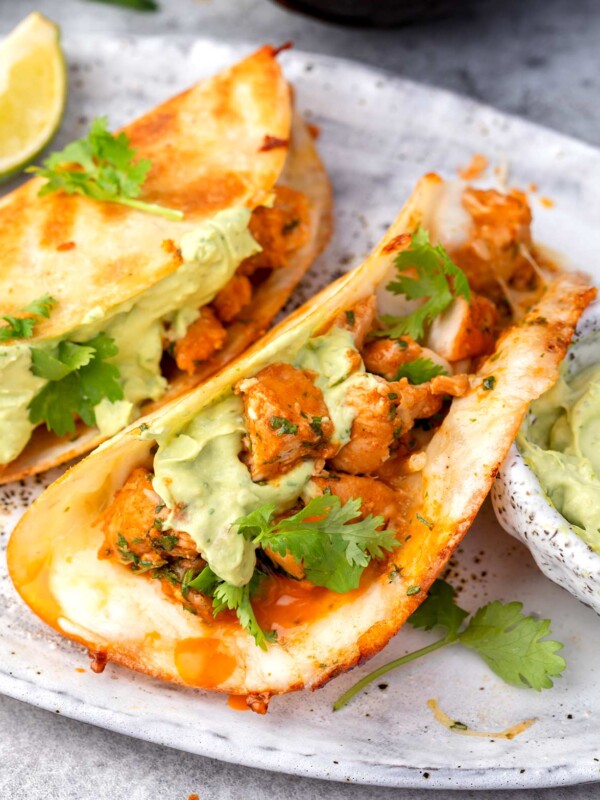 Crispy buffalo chicken tacos with avocado crema and fresh cilantro on a plate.