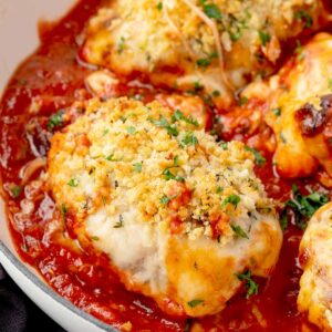 Close-up of baked chicken parmesan casserole topped with golden crispy breadcrumbs, melted cheese, and fresh parsley in a skillet with rich marinara sauce.
