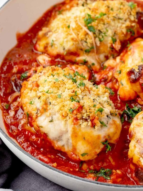 Close-up of baked chicken parmesan casserole topped with golden crispy breadcrumbs, melted cheese, and fresh parsley in a skillet with rich marinara sauce.