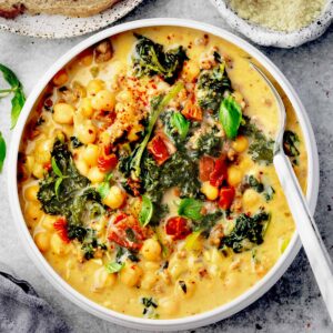 Creamy Tuscan chickpea soup with kale, sun-dried tomatoes, and Italian sausage served in a white bowl.