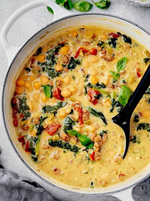 One-pot creamy Tuscan chickpea soup with sausage, kale, and sun-dried tomatoes in a white Dutch oven.