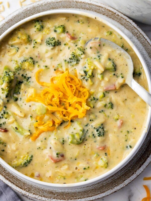 Bowl of creamy broccoli cheddar orzo soup topped with shredded cheddar cheese and served with a spoon.