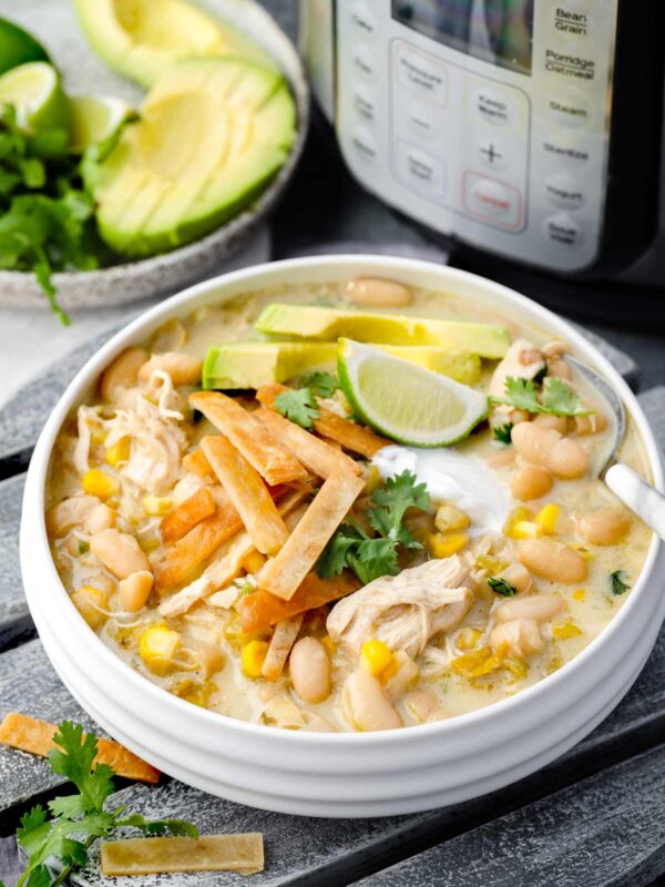 Bowl of Instant Pot White Chicken Chili with shredded chicken, white beans, corn, tortilla strips, avocado, lime, and cilantro garnish.