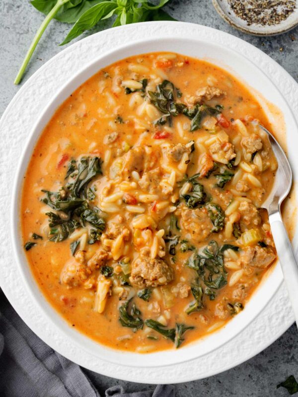 Creamy Italian sausage and orzo soup in a white bowl, topped with kale, tomatoes, and herbs โ a hearty, comforting one-pot meal perfect for cold days.
