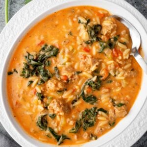 Creamy Italian sausage and orzo soup in a white bowl, topped with kale, tomatoes, and herbs โ a hearty, comforting one-pot meal perfect for cold days.