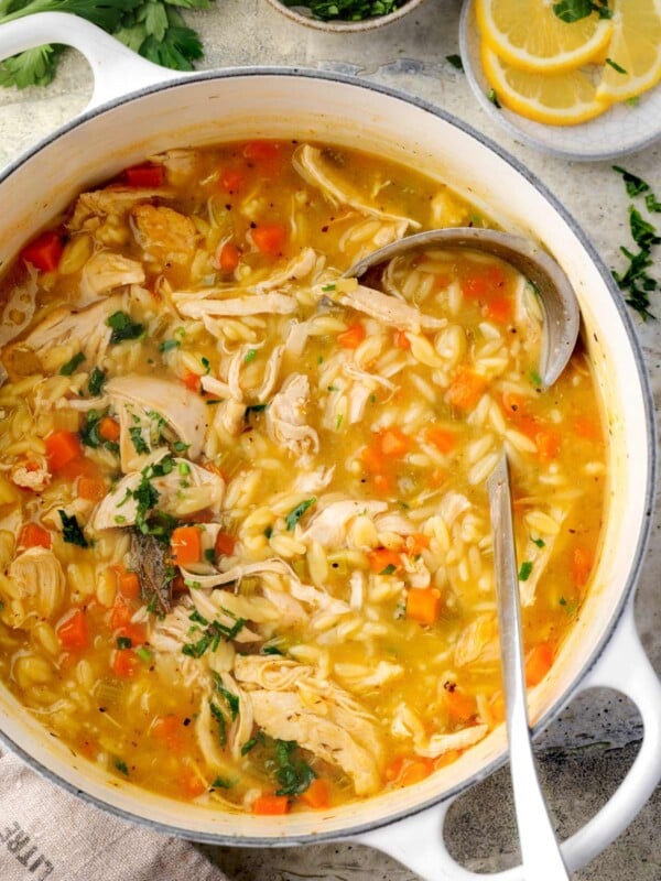 Homemade lemon chicken orzo soup in a white pot with shredded chicken, carrots, celery, and orzo pasta in a golden broth, garnished with fresh parsley and lemon slices on the side.