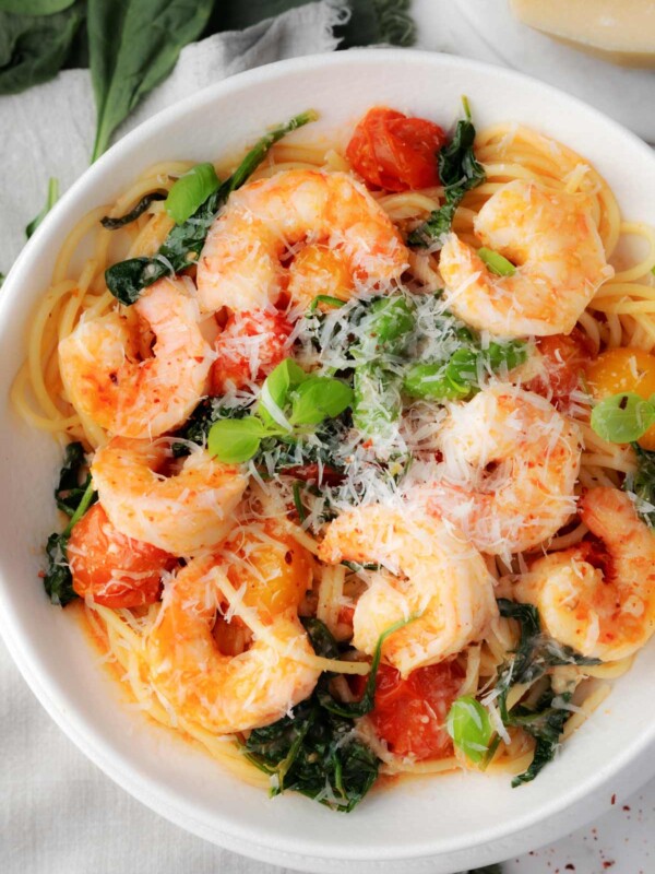 Bowl of pasta with shrimp, cherry tomatoes, and fresh spinach topped with grated Parmesan and basil โ easy shrimp pasta recipe with tomatoes and spinach.