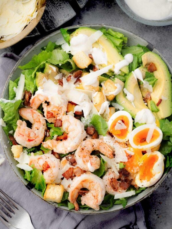 Shrimp Caesar Salad with avocado, soft-boiled eggs, bacon, croutons, and Parmesan, topped with creamy Caesar dressing.
