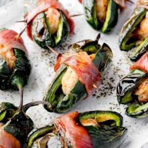 Close-up of bacon-wrapped shrimp stuffed jalapeรฑos on a white plate, showing crispy bacon, charred peppers, and juicy shrimp filling โ easy spicy appetizer recipe.