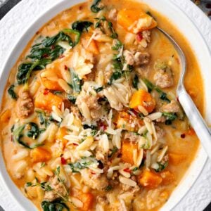 Butternut Squash and Sausage Orzo Soup topped with spinach, Parmesan cheese, and thyme in a white bowl.