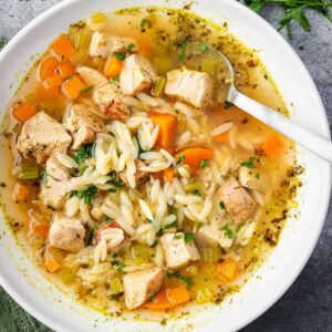 A comforting bowl of turkey orzo soup filled with tender chunks of turkey, orzo pasta, carrots, celery, and herbs in a clear golden broth โ served with a spoon and garnished with fresh parsley.