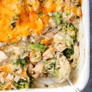 Easy 5-ingredient chicken broccoli casserole with rice, tender chicken pieces, and broccoli, topped with melted cheddar cheese in a white baking dish.