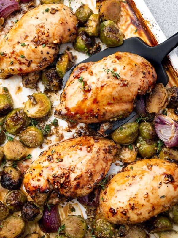 Sheet pan balsamic chicken breasts with roasted Brussels sprouts and red onions, glazed with honey balsamic sauce and fresh thyme.