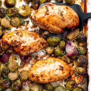 Sheet pan balsamic chicken breasts with roasted Brussels sprouts and red onions, caramelized in a garlic honey balsamic glaze and garnished with fresh thyme.