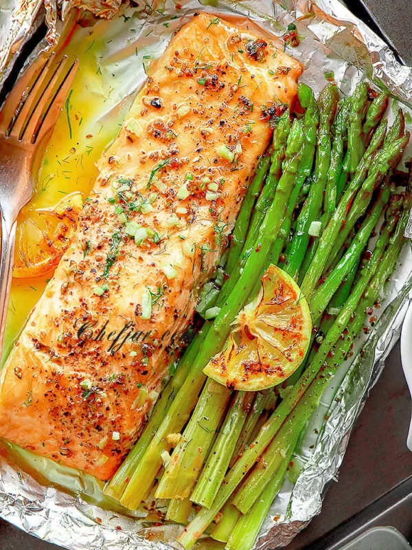 Baked salmon fillet cooked in foil with asparagus, lemon, and herbs, showing a healthy sheet pan salmon dinner ready to serve.