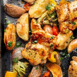 Close-up of sheet pan garlic herb chicken thighs roasted with golden potatoes, broccoli, bell peppers, and red onion, finished with fresh herbs for a flavorful one-pan dinner.