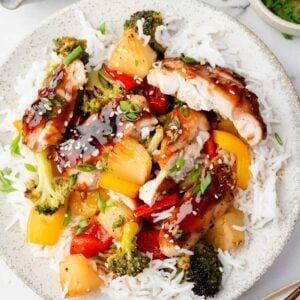Sheet pan teriyaki chicken served over white rice with roasted broccoli, bell peppers, and pineapple, drizzled with homemade teriyaki sauce and topped with sesame seeds and green onions.
