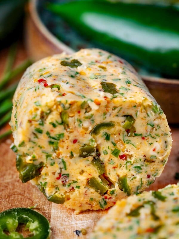 Roasted jalapeรฑo cowboy butter log with fresh herbs and spices, sliced on a wooden board.