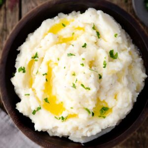Bowl of creamy cottage cheese mashed potatoes topped with melted butter, cracked black pepper, and fresh parsley.