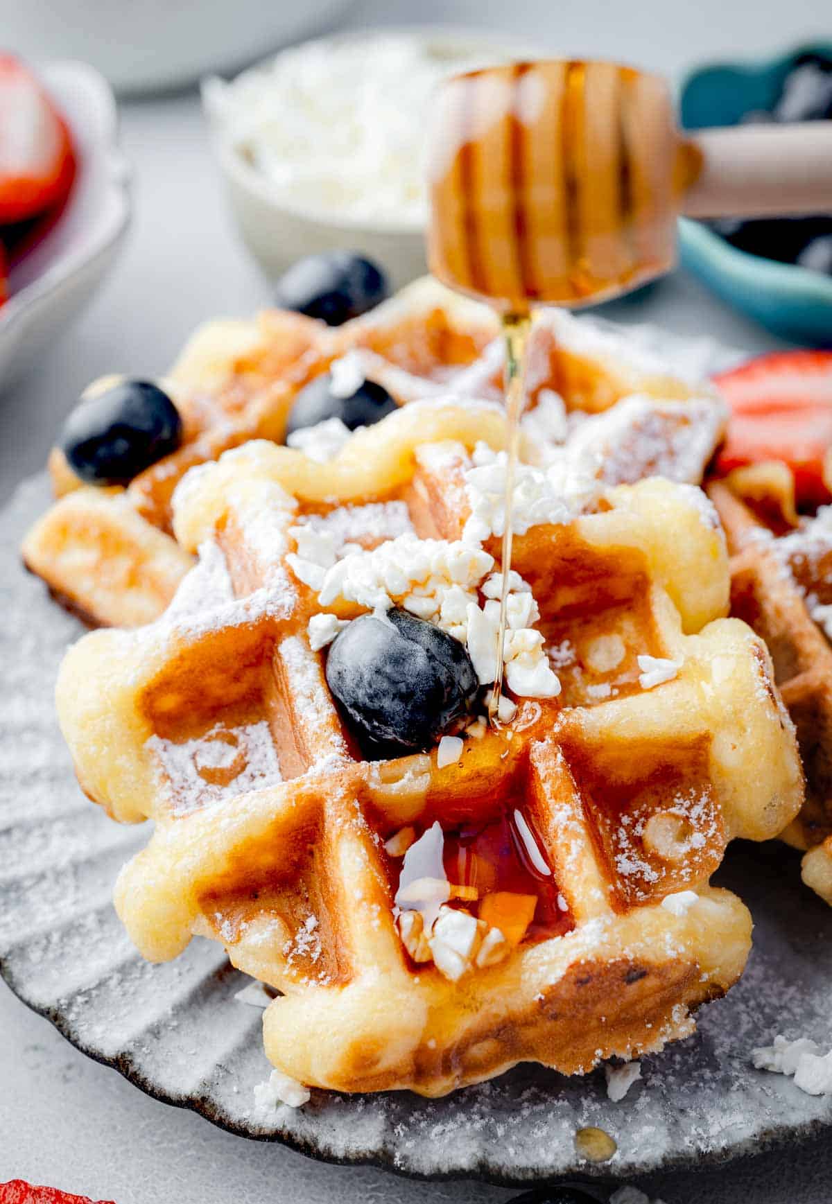 Cottage cheese waffles topped with fresh blueberries, crumbled cottage cheese, powdered sugar, and honey drizzle on a plate.
