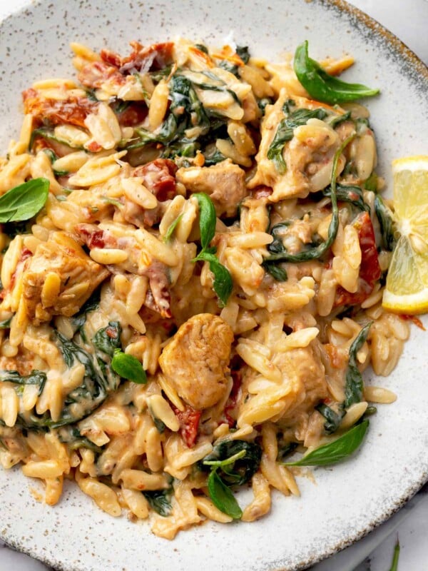 Creamy marry me chicken orzo with sun-dried tomatoes and spinach on a white plate.
