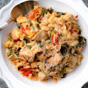 Creamy Boursin chicken orzo bake served on a white plate with spinach, cherry tomatoes, tender chicken, and grated Parmesan cheese.