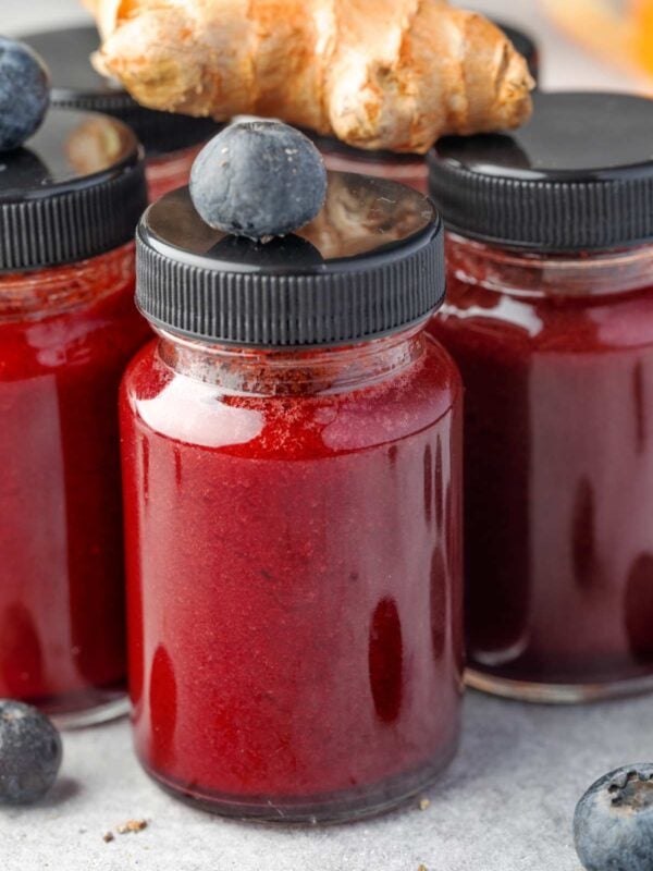 Homemade blueberry lemon ginger shots in small glass bottles, vibrant red wellness drink with fresh blueberries and ginger.
