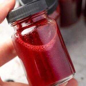 Close-up of a blueberry lemon wellness shot in a small glass bottle, vibrant red homemade drink with fresh blueberries and citrus.