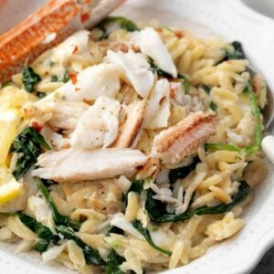 Creamy Boursin crab orzo with spinach and lemon, topped with tender crab meat and a crab claw, served on a white plate.