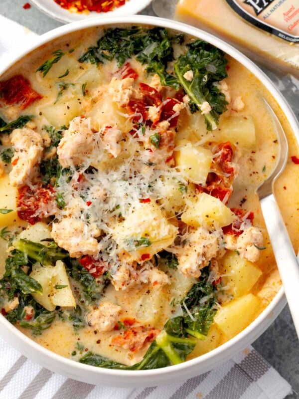 Creamy Tuscan chicken potato soup with kale, sun-dried tomatoes, tender potatoes, and grated Parmesan cheese in a white bowl.