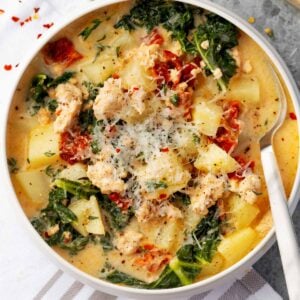 Creamy Tuscan chicken potato soup with kale, sun-dried tomatoes, and grated Parmesan cheese in a white bowl.