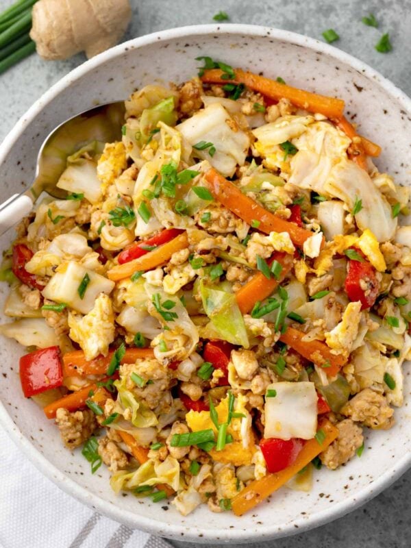 Chicken and cabbage stir fry with carrots, bell peppers, scrambled eggs, and green onions in a bowl, healthy one-pan Asian-style meal.