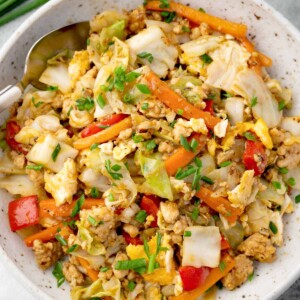 Chicken and cabbage stir fry with carrots, bell peppers, scrambled eggs, and green onions in a bowl, healthy one-pan Asian-style meal.