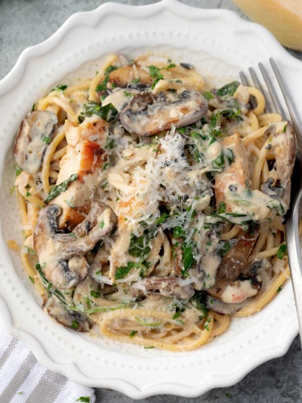 Creamy chicken and mushroom pasta with spaghetti, fresh spinach, and grated Parmesan cheese in a white bowl, topped with parsley and rich garlic cream sauce.