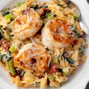 Creamy shrimp orzo with sun-dried tomatoes, asparagus, and spinach in a white bowl topped with grated Parmesan.