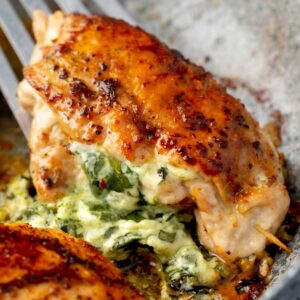 Golden pan-seared spinach stuffed chicken breast in skillet, filled with creamy melted cheese and herbs, showing juicy interior and crispy caramelized top.