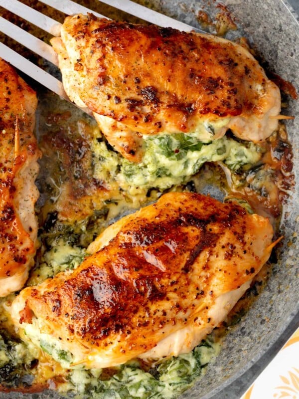 Golden-brown spinach stuffed chicken breasts in a skillet, filled with creamy spinach and cheese, pan-seared until juicy and caramelized on top.