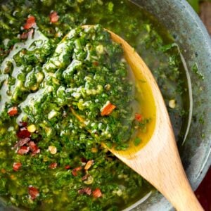 Fresh cilantro chimichurri sauce with garlic, olive oil, and red pepper flakes in a bowl, served with a wooden spoon, vibrant green herb sauce close-up.