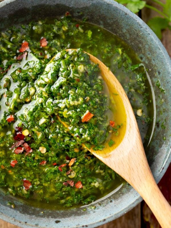 Fresh cilantro chimichurri sauce with garlic, olive oil, and red pepper flakes in a bowl, served with a wooden spoon, vibrant green herb sauce close-up.