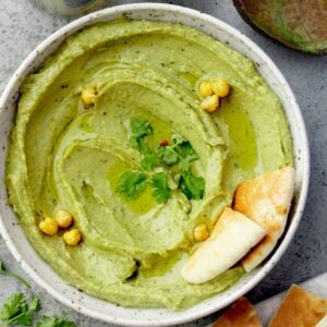 Creamy avocado hummus topped with olive oil, chickpeas, and fresh cilantro, served with pita bread.